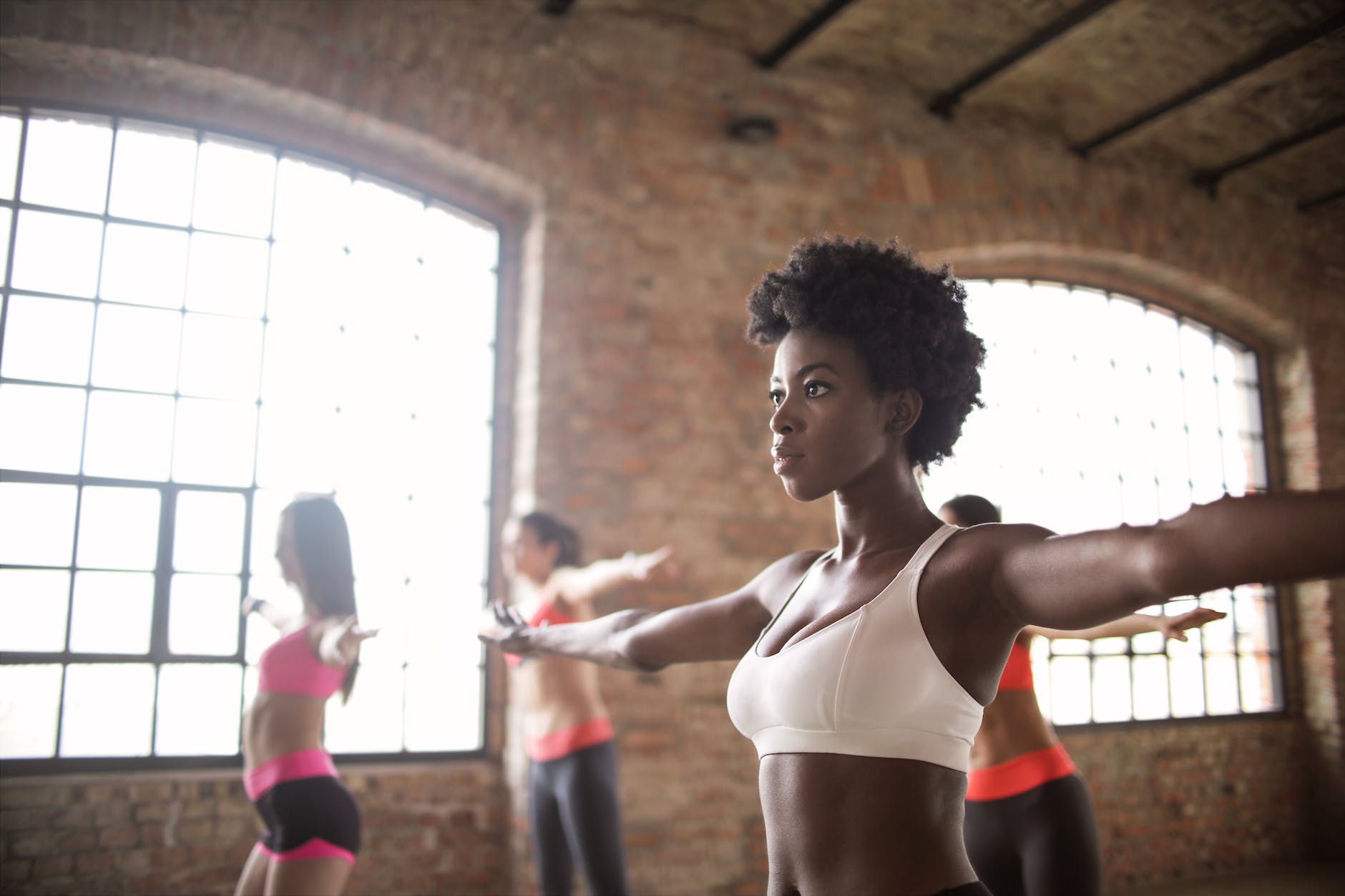 confident fit ethnic woman training with other sportswomen in modern fitness studio