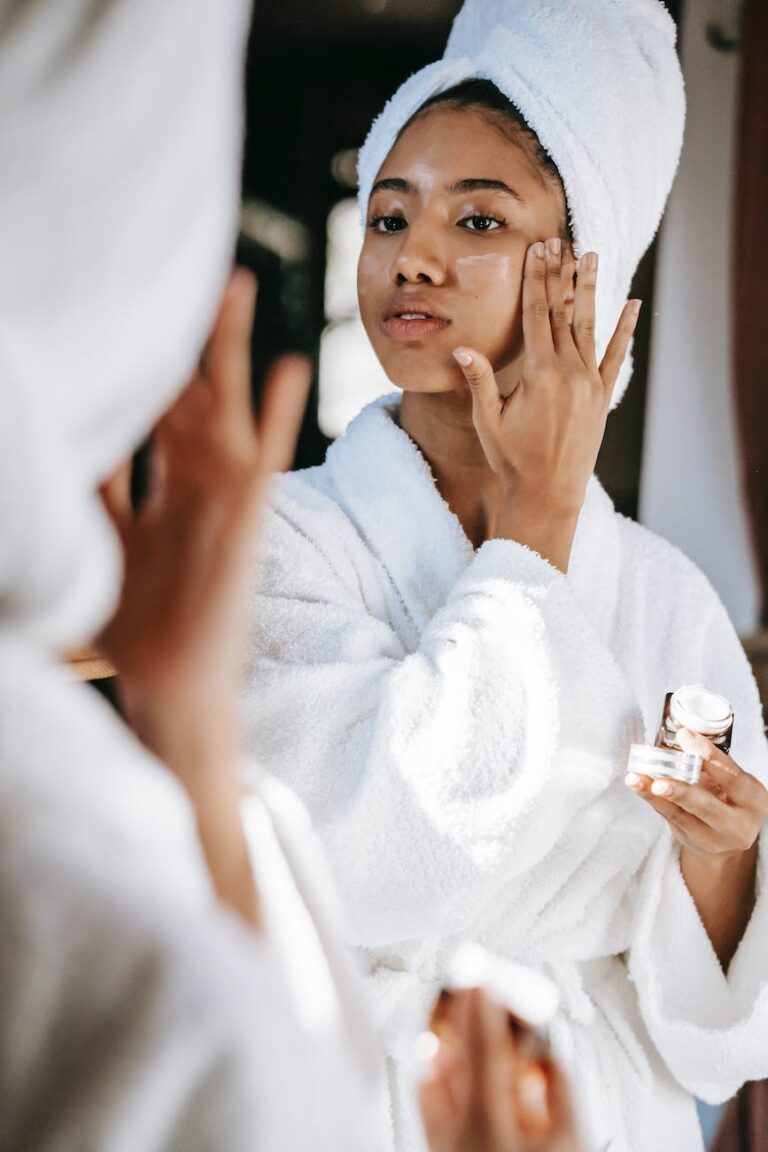 black woman with towel applying cream on face