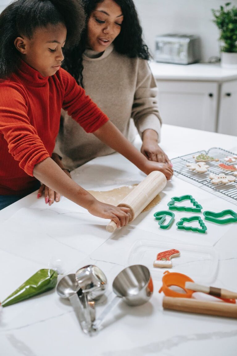 crop black girl rolling out dough while helping mother