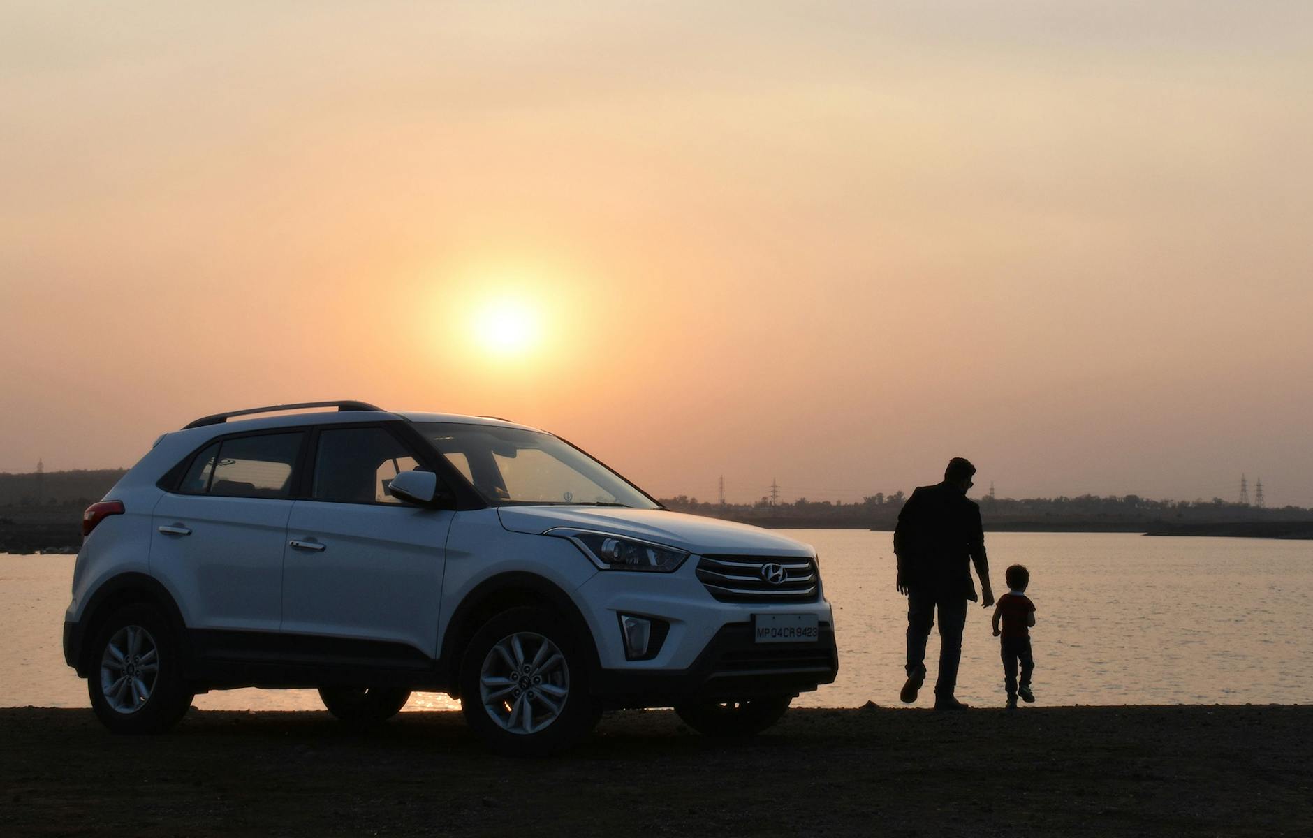 silhouette of man and child near white hyundai tucson suv during golden hour