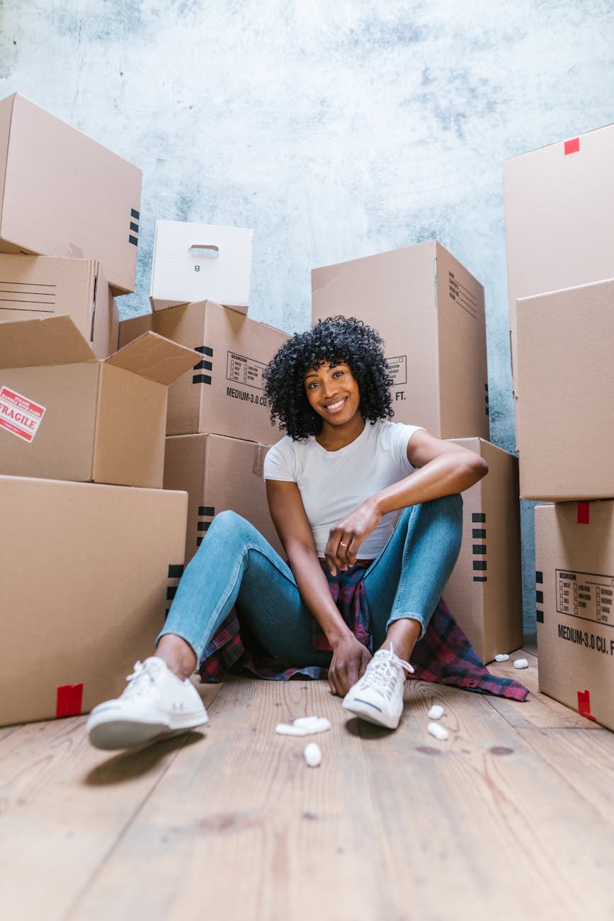 woman in white tank top and blue denim jeans sitting on brown cardboard box