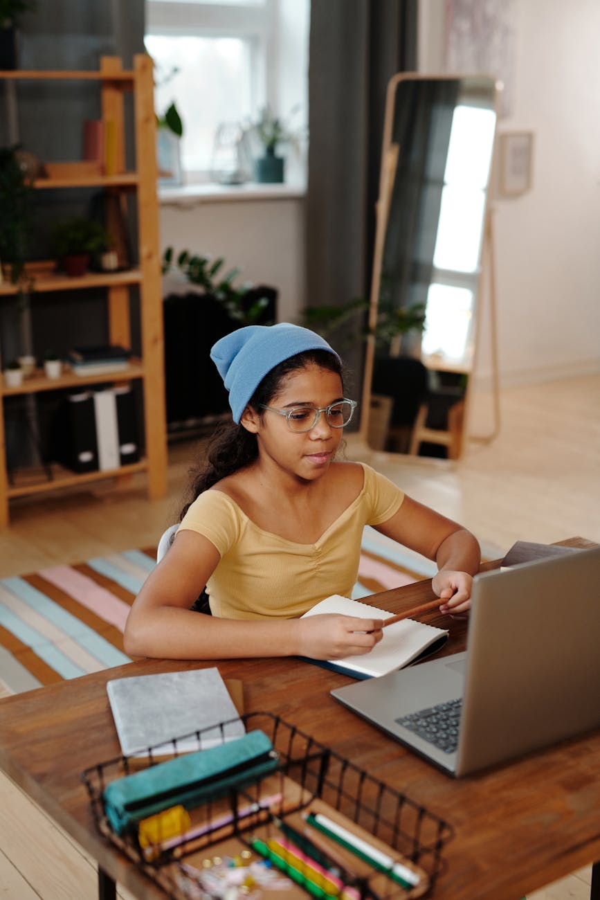 a girl in yellow top wearing beanie while looking at the laptop